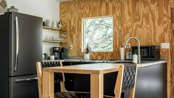 A modern kitchen with a wooden island, black appliances, and a view of trees through a window.