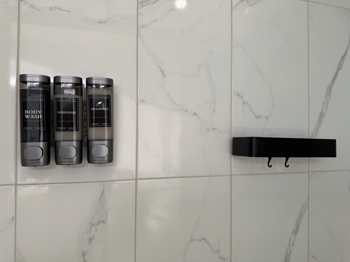 Een badkamer met drie toiletartikelen op een plank en een zwarte handdoekhouder.