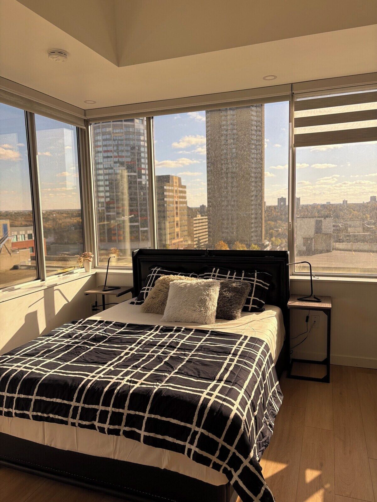 A bedroom with a large bed, a nightstand, and a window with a city view.