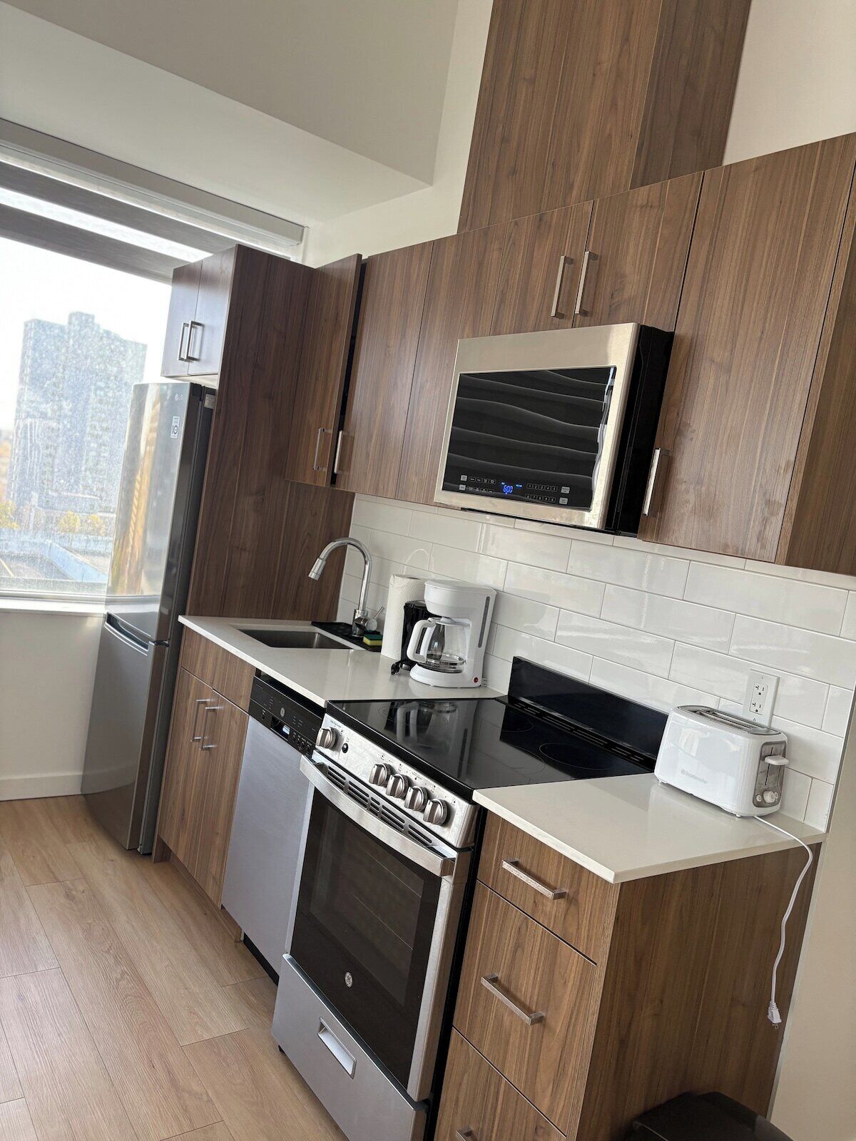 Una cucina moderna con elettrodomestici in acciaio inossidabile, mobili in legno e una finestra che offre vista sulla città.