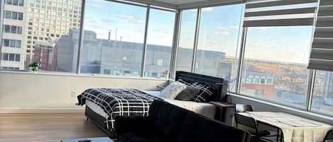 Amplia sala de estar con una cama grande, un sofá negro, una mesita y un comedor con mesa y sillas.