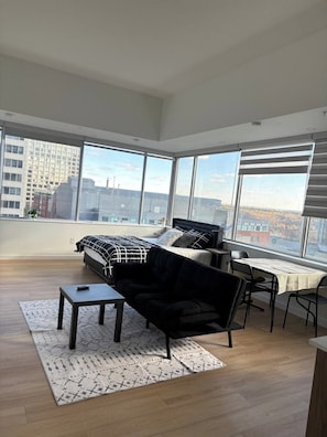 Uma sala de estar espaçosa com uma cama grande, um sofá preto, uma mesa pequena e um espaço de jantar com mesa e cadeiras.