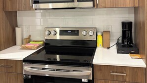 A kitchen with wooden cabinets, a stainless steel microwave, an oven, and a coffee maker. - One-Bedroom Executive Stay | Central & Convenient (Edmonton)