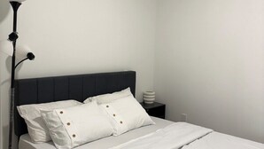 A bedroom with a bed, a nightstand, and a floor lamp. - One-Bedroom Executive Stay | Central & Convenient (Edmonton)