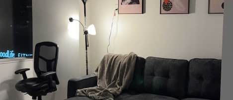 Un salon moderne avec un canapé d’angle, une table basse ronde, un lampadaire et des œuvres d’art abstraites accrochées au mur.