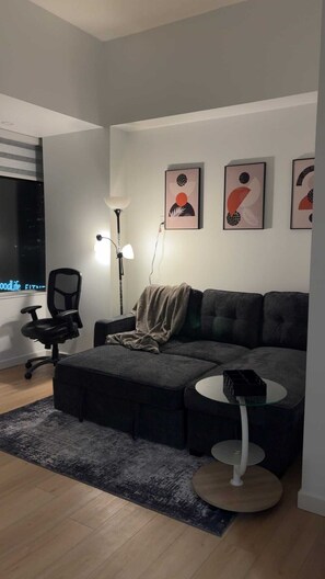 A modern living room with a sectional sofa, a round coffee table, a floor lamp, and abstract wall art. - One-Bedroom Executive Stay | Central & Convenient (Edmonton)