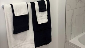 A bathroom with a white tiled wall, a white bathtub, and a towel rack with two towels. - One-Bedroom Executive Stay | Central & Convenient (Edmonton)