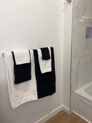 Ein Badezimmer mit weiß geflieste Wand, einer weißen Badewanne und einem Handtuchhalter mit zwei Handtüchern.