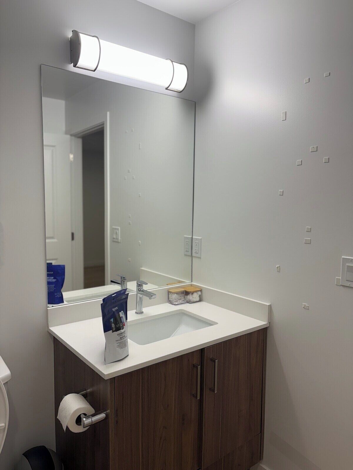 Een badkamer met een witte wasbak, een spiegel, een toilet en een rol toiletpapier.
