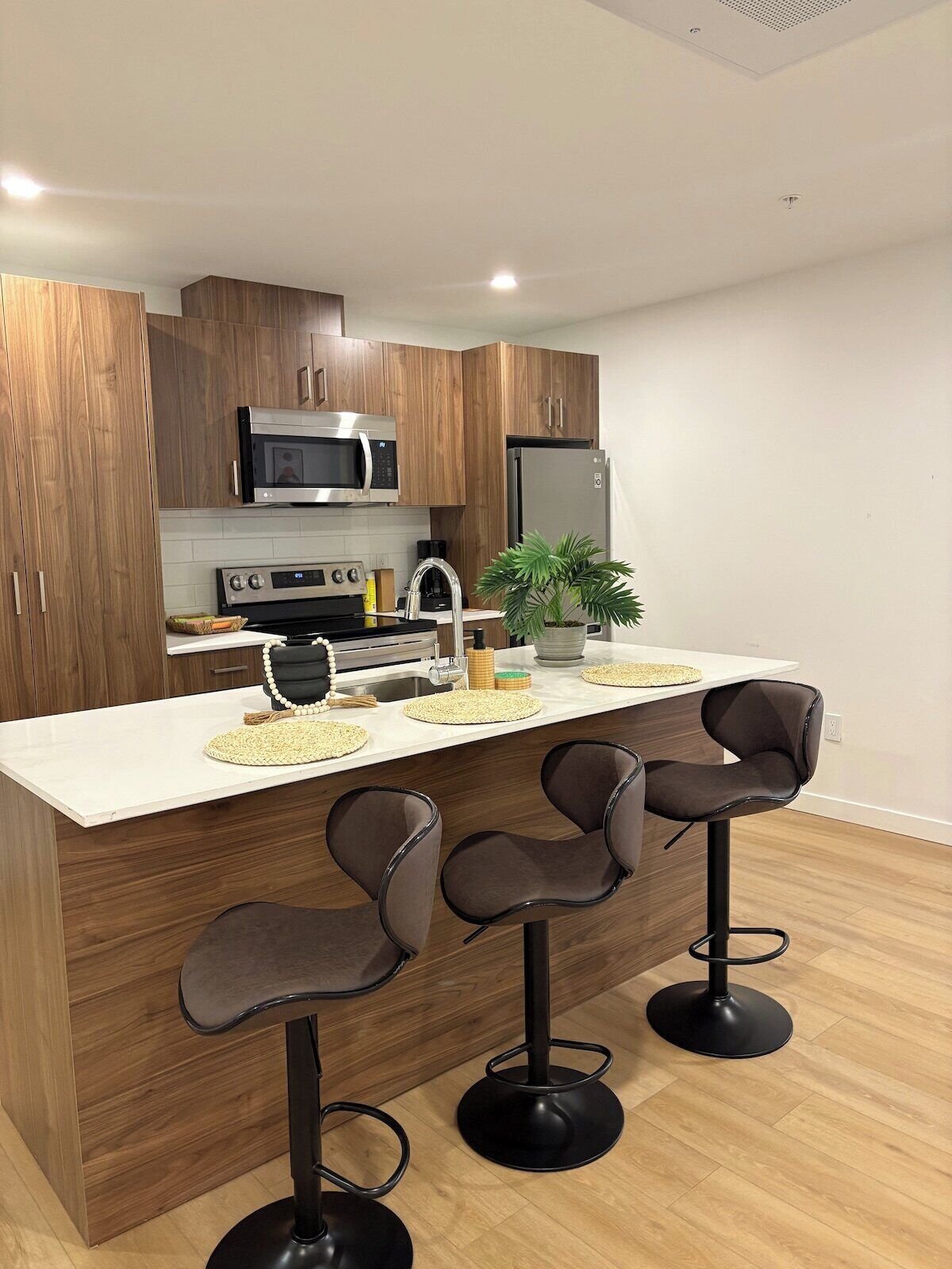 Una cocina moderna con armarios de madera, electrodomésticos de acero inoxidable, una isla central con taburetes y una planta en maceta.