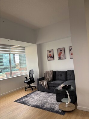 A modern living room with a grey sofa, a glass coffee table, and a black office chair. - One-Bedroom Executive Stay | Central & Convenient (Edmonton)