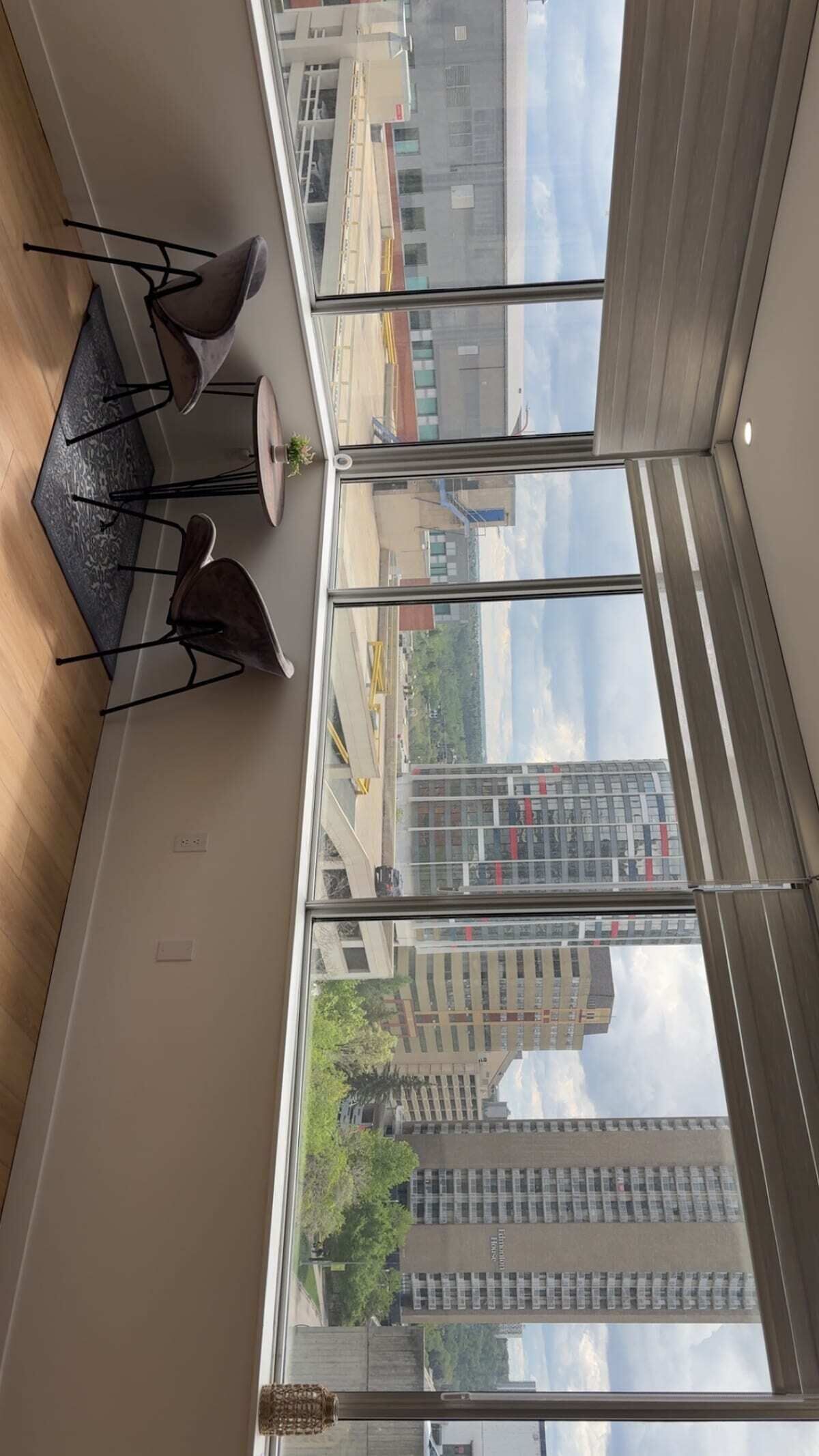 Ein Zimmer mit großem Fenster, einem Esstisch mit Stühlen und Blick auf eine Stadtlandschaft.