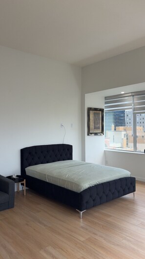 Ein modernes Schlafzimmer mit einem großen Bett, einem kleinen Nachttisch und einem Fenster mit Blick auf die Stadt.