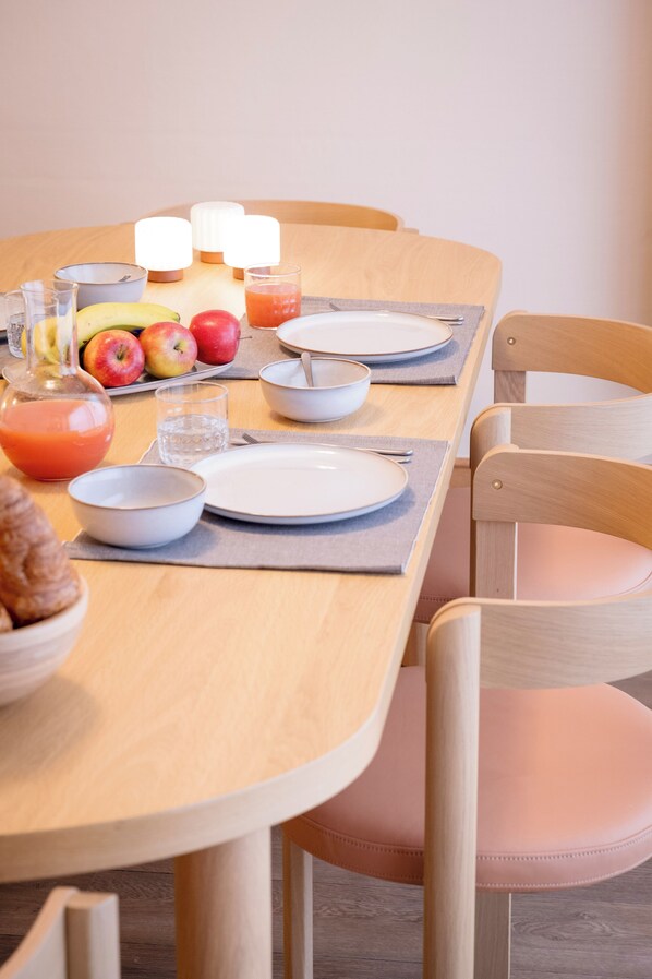Una mesa de comedor dispuesta con platos, tazones, vasos y una cesta de frutas.