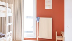 Une pièce avec un lit superposé, un radiateur, une table et une fenêtre avec des rideaux.
