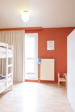 A room with a bunk bed, a radiator, a table, and a window with curtains. - La Petite Crevette: Beach and Charm in De Haan (De Haan)