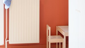 Une pièce avec un radiateur, un tableau encadré accroché au mur, un bonnet bleu posé sur le radiateur et une table en bois avec une chaise.