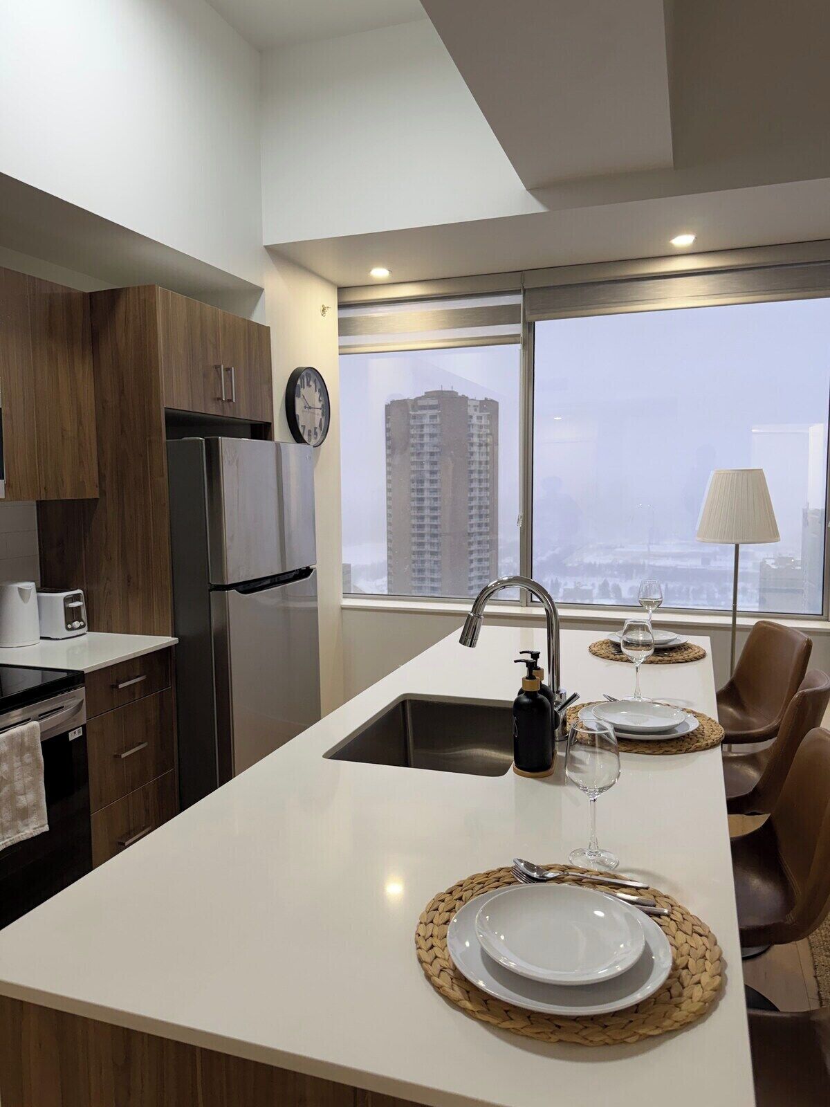 A modern kitchen with a central island, stainless steel appliances, and a view of a cityscape through large windows.