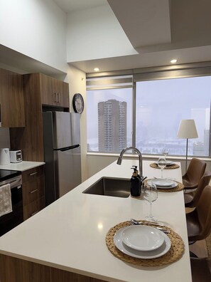 A modern kitchen with a central island, stainless steel appliances, and a view of a cityscape through large windows. - Downtown Gem 2BR Apartment with Stunning City View (Edmonton)