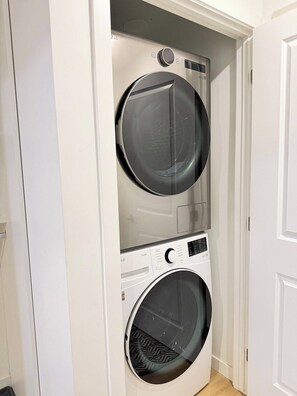 A compact, wall-mounted laundry machine with a control panel and a circular door, installed in a narrow hallway. - Downtown Gem 2BR Apartment with Stunning City View (Edmonton)