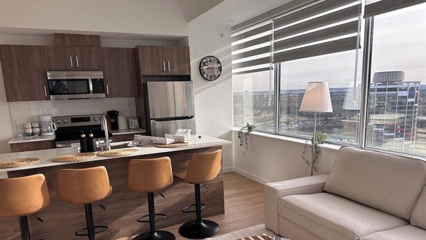 Eine moderne Küche mit Kochinsel, Barhocker und einer Couch im Wohnbereich mit Blick auf die Stadt.