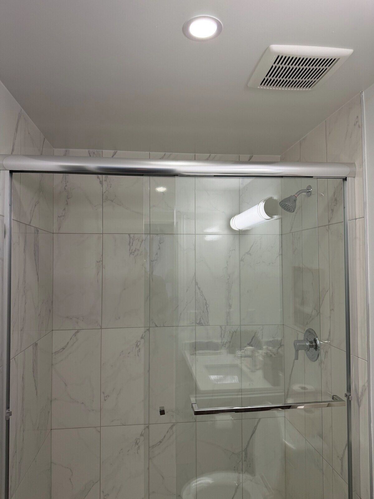 A modern shower enclosure with a glass door, a showerhead, and a control panel.