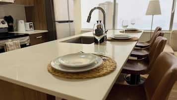 A modern kitchen with a central island, a built-in sink, and a dining area with chairs and a table set for two.