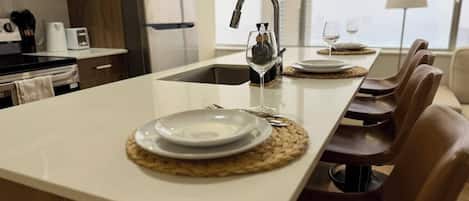 Une cuisine moderne dotée d’un îlot central, d’un évier intégré et d’un coin repas avec des chaises et une table préparée pour deux personnes.