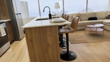 Una cocina moderna con una isla central, taburetes de bar, un área de comedor con sofá y vistas a la ciudad a través de amplios ventanales.