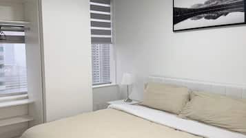 A bedroom with a bed, a window with blinds, a nightstand with a lamp, and a framed picture on the wall.