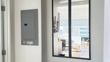 A room with a white wall, a door, a window with a view of a cityscape, and a shelf with a book.