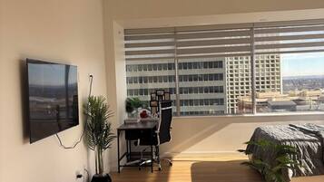 A modern living room with a large window, a flat-screen TV, a desk, and a comfortable seating area.