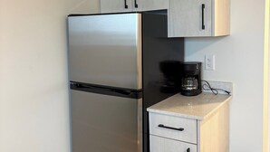 A compact kitchen with a stainless steel refrigerator, a coffee maker on the countertop, and a black trash bin. - Executive Studio Near Rogers Place” (Edmonton)