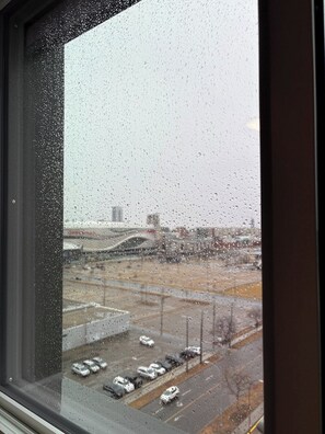 A view through a window with raindrops, featuring a parking lot with several cars and a bridge in the background. - Executive Studio Near Rogers Place” (Edmonton)