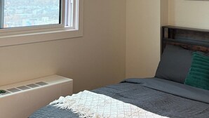 A bedroom with a bed, a window, a radiator, and a wall-mounted artwork. - Executive Studio Near Rogers Place” (Edmonton)