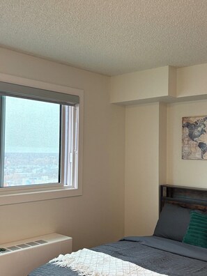A bedroom with a bed, a window, a radiator, and a wall-mounted artwork. - Executive Studio Near Rogers Place” (Edmonton)