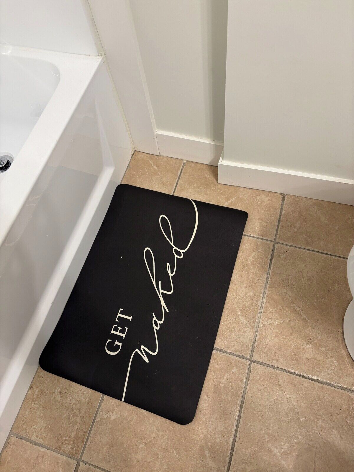 A bathroom with a black mat on the floor that reads 'GET Married.'