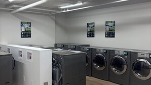 A laundry facility with multiple washing machines and dryers, fluorescent lighting, and signs on the walls. - unique small studio apartment close to roger’s (Edmonton)