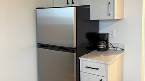 A compact kitchen with a stainless steel refrigerator, a coffee maker, and a trash bin. - unique small studio apartment close to roger’s (Edmonton)