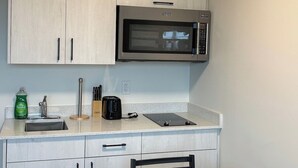 A compact kitchen with white cabinets, a microwave, a sink, and a dining table with chairs. - unique small studio apartment close to roger’s (Edmonton)
