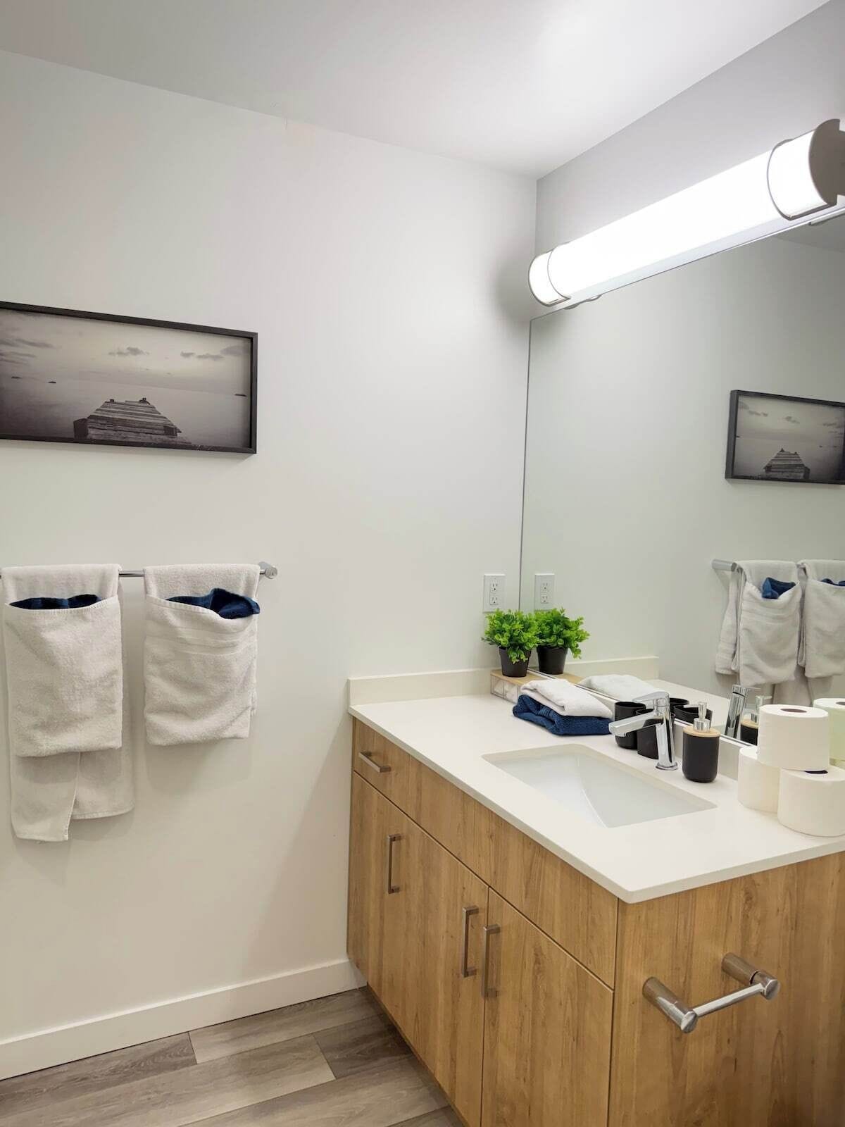 A modern bathroom with a wooden cabinet, a white sink, and two framed pictures on the wall.