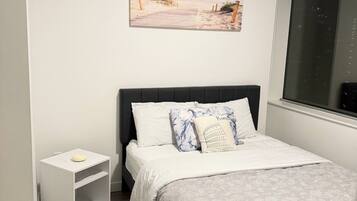 A bedroom with a bed, a nightstand, a picture on the wall, and a window.