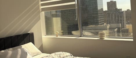 Une chambre à coucher avec un lit, une fenêtre avec des stores et une vue sur la ville.