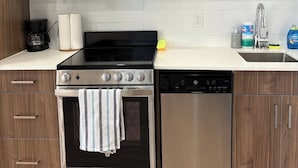 A modern kitchen with stainless steel appliances, wooden cabinets, and a white countertop. - small cozy studio apartment (Edmonton)
