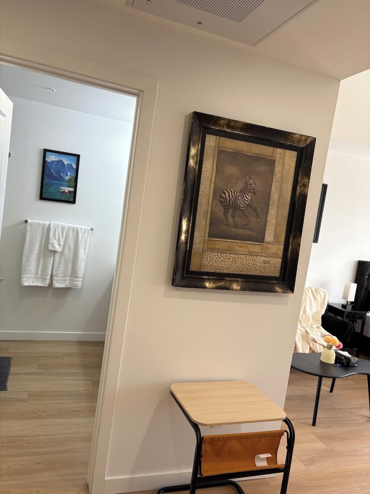 A room with a wooden desk, a framed artwork, a towel rack, and a painting on the wall.