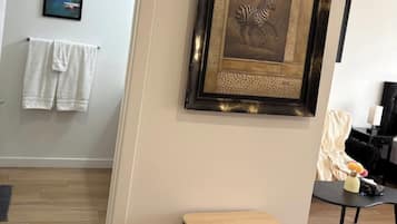 A room with a wooden desk, a framed artwork, a towel rack, and a painting on the wall.