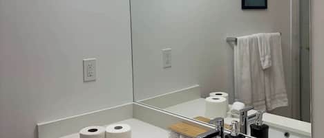 A modern bathroom with a large mirror, a sink, and two rolls of toilet paper on the counter.