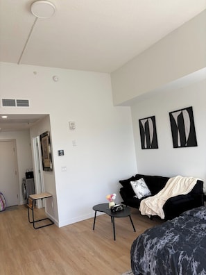Ein modernes Wohnzimmer mit einem schwarzen Sofa, einem kleinen Tisch und einem Bett mit dunkel gemustertem Bezug.