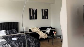 A modern bedroom with a large bed, a sofa, and a small table. There are two abstract paintings on the wall.