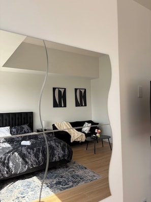 Ein modernes Schlafzimmer mit einem großen Bett, einer Couch und einem kleinen Tisch. An den Wänden hängen zwei abstrakte Gemälde.